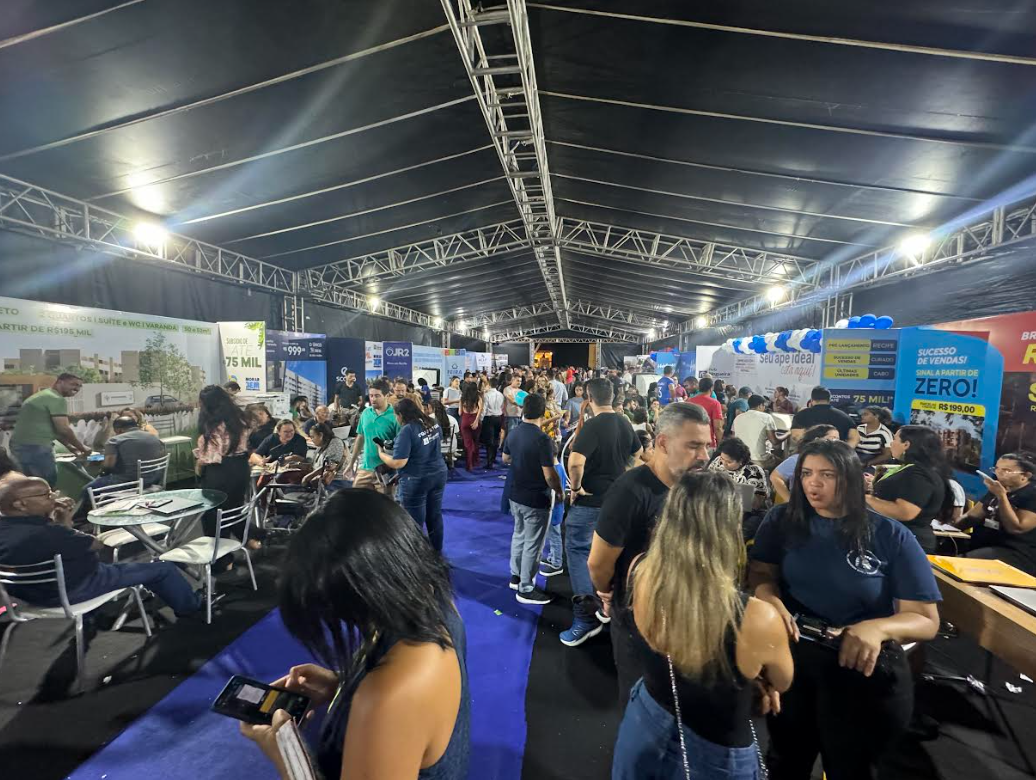 Pessoas sentadas ao redor de mesas e em pé no salão feira de negócios